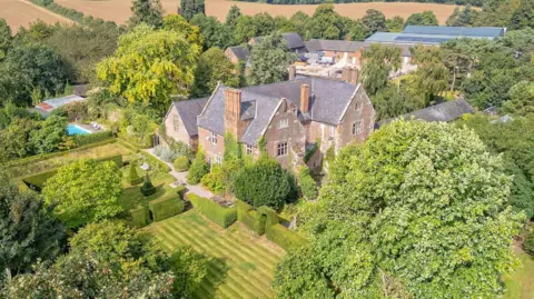 Savills An aerial view of a large Elizabethan house, surrounded by green fields and woodland
