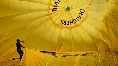 Getty Images A man stands inside the canopy of a yellow Thatchers hot air balloon