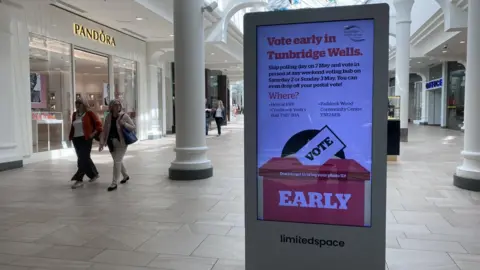 Interior of shopping centre showing two people walking past an electronic display board