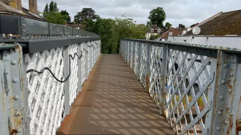 Vikki Irwin/BBC A view along the top of a footbridge. It is lined with metal fences and there are black handrails on both sides.