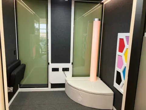 Room with soft bench and seat and coloured shapes on one wall.