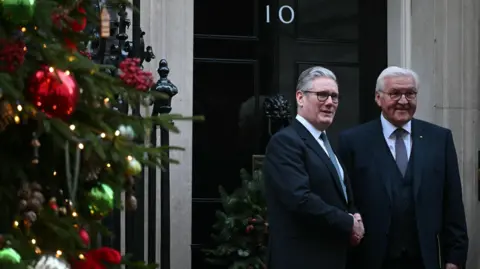 PA Media Sir Keir Starmer greets President Steinmeier outside No 10 Downing Street. Both men are shaking hands and posing for a photograph, with a Christmas tree decorated in red and green off to the left of the frame.