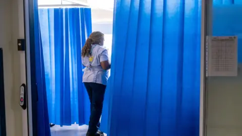 A nurse walks through several hospital blue curtains.