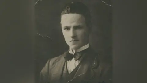 A black and white photograph of Hector MacDonald Graham. He has his hair brushed back and is wearing a suit with a bow tie and is looking at the camera.