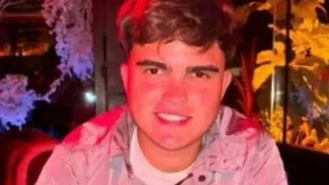 Luke Miller smiling at the camera in a room that is decorated with purple and yellow flowers 