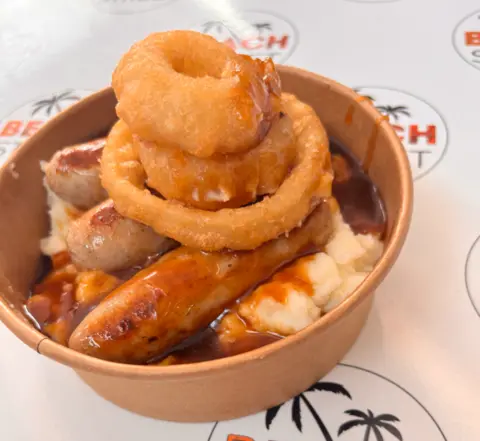 Charlie Pearson Cardboard dish containing sausages, mash and onion rings