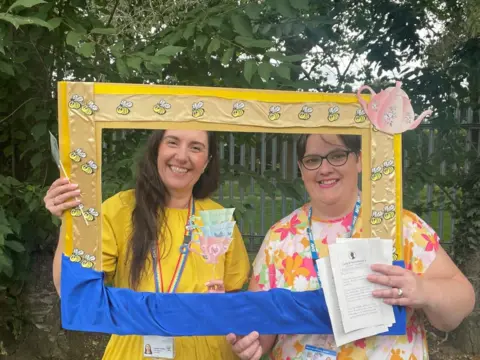 Attendees smile while holding a yellow and white decorated frame with bees 