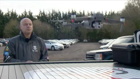 Phil James flying a drone as it takes off, with cars parked in the background