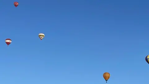 Laura Foster/BBC  Four colourful balloons float in the sky on a clear blue day. 