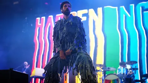 PA Media Serge Pizzorno from Kasabian. He has short dark hair and facial hair. He is pictured on stage, looking out at the crowd