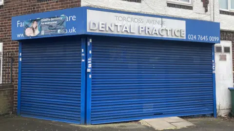 The exterior of Torcross Dental practice with the name in white letters and blue shutters