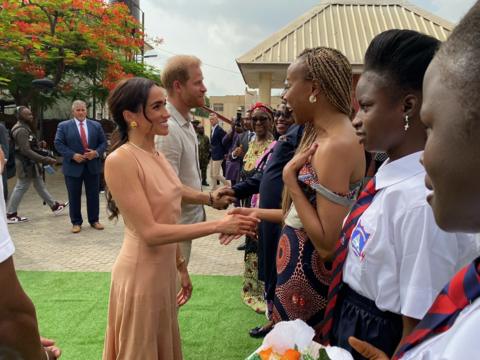 Prince Harry and Meghan shaking hands with a line of people outside a school in Abuja, Nigeria.