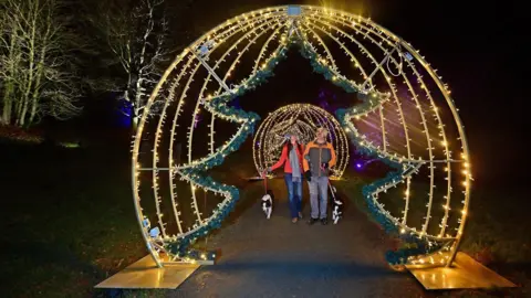 Bedgebury National Pinetum A couple walking through a Christmas trail with festive lights.