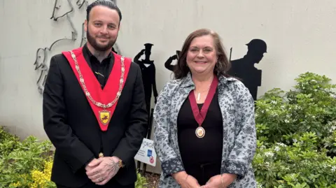 Warminster Town Council Two people wearing medals and smiling widely at the camera. One is a young man and the other is an older woman.