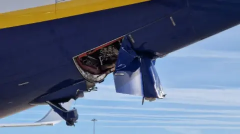 AAIB The rear of the blue, yellow and white aircraft has been damaged. Part of it has been peeled and is hanging off. Mechanics have been exposed as a result.