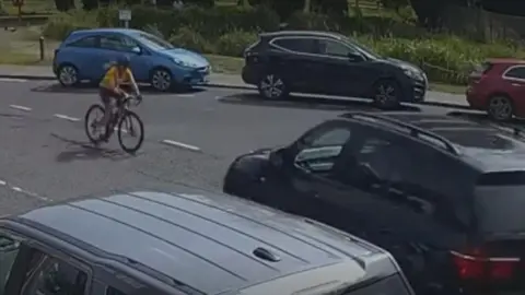 Thames Valley Police Cylclist in yellow surrounded by cars. She is heading from left to right.