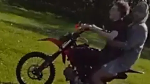 West Midlands Police A photograph taken from police bodyworn video showing two young men on a scrambler bike in Stowlawn Green. The one on the front of the bike is holding the handlebars and looking straight forwards. He is wearing a black T-shirt and black trousers and trainers. The other sitting behind him is wearing shorts and trainers and a grey hoodie and he has turned his head to look at the person taking the image.