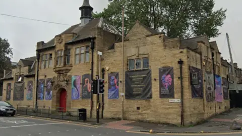 A photo of a beige stone building on a street corner. Along its walls are many black, white and blue advertising banners.