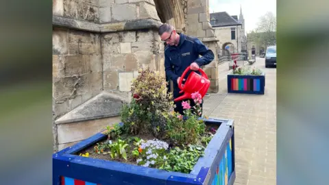 Peterborough Positive Terry watering a wooden planter - with a red watering can 