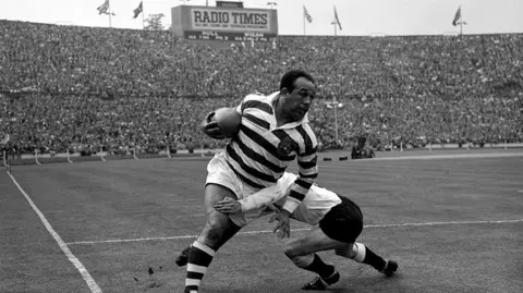 PA Media Billy Boston during the 1959 Rugby League Challenge Cup Final.Legendary rugby league star Billy Boston (Wigan) bursts through despite a tackle by I. Watts (Hull) during the Rugby League Challenge Cup Final at Wembley with huge crowds watching on.