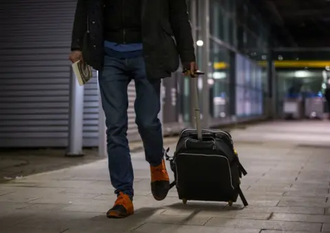 A passenger wheels a suitcase while walking out of the airport. 