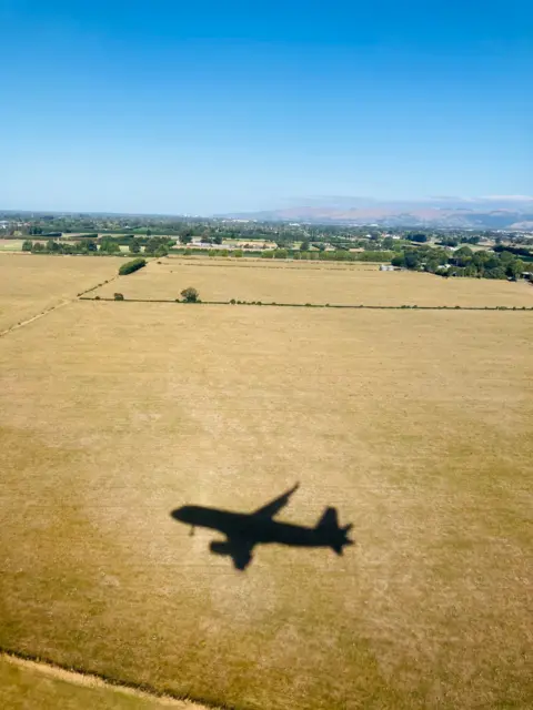 Karen Faiers The shadow of an aeroplane as it flies over a field