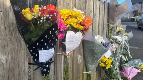 Flowers tied to a wooden fence with notes on them