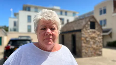 Mary Young looks at the camera. She has short white hair, and is wearing a white tshirt.