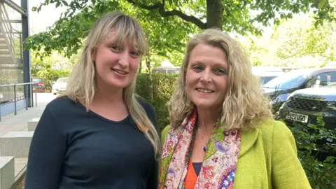 Emma Howgego/BBC Yasmin, on the left, wears a black top, she has long blonde hair. On the right Natalie has shoulder-length blonde hair. She wears a green jacket with a colourful scarf.
