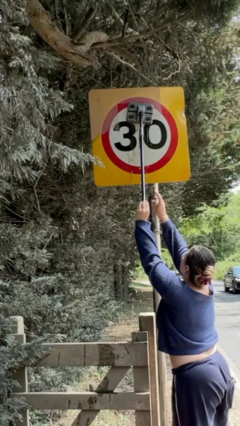 Woman reaches up to clean a 30mph sign with a mop.
