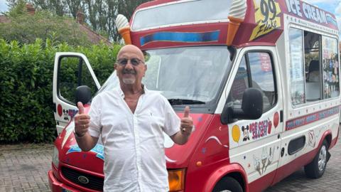 Mr Shaouna stood wearing a white shirt and a gold chain, holding two thumbs up, in front of his red and white van. 