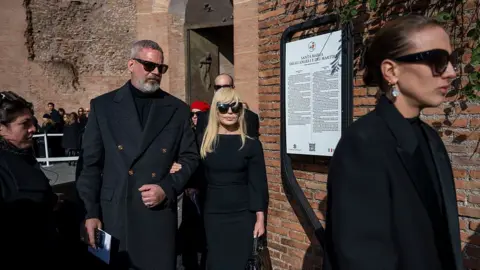 Antonio Masiello/Getty Images Donatella Versace, dressed in black and wearing sunglasses, leaves the funeral ceremony accompanied by others