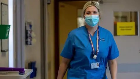 Getty Images A NHS staff member walking down a corridor wearing a mask and blue scrubs