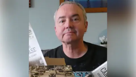 Richard Pursehouse A man with short grey hair smiles at the camera while sitting in a room.