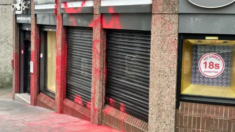 Red paint seen on shopfront with some on the pavement outside