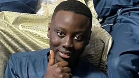 Greater Manchester Police A young teenager sits smiling and giving a thumbs up to the camera. 