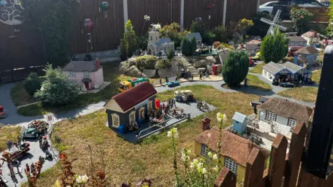 Jack Maclean/BBC The model village with about 20 tiny properties in Jane High's front garden at her home in Scratby. Within the picture there are many miniature figures that populate the scene. 