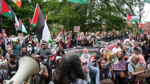 A large group of protesters outside Woolwich Crown Court. Many of them are holding flags and banners in support of Palestine Action.