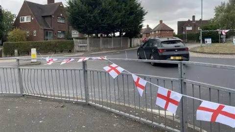 BBC A string of flags on a roundabout. In the background is a black car