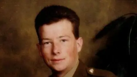 Doreen Savage Adam Savage smiles at the camera. He has short dark hair and wears an army uniform.