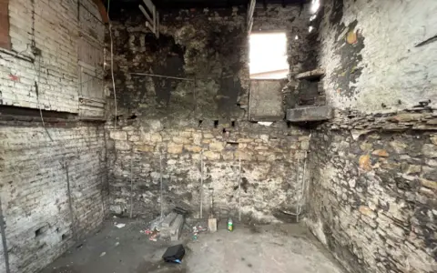 Auction House South Yorkshire The inside of a building with stone walls and exposed wires. There's rubbish on the concrete floor.
