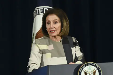 Getty Images Nancy Pelosi delivers remarks at an award ceremony in Washington DC on 9 December. She has a brown bob hair-cut and wears a patterned blouse.