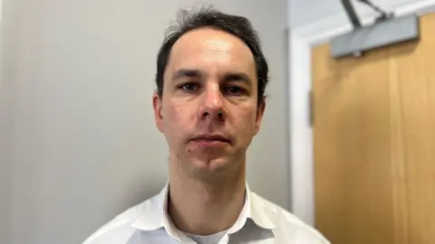 Porchlight Chief Executive, Tom Neumark. Tom is stood to camera, has dark hair and is wearing a white shirt.