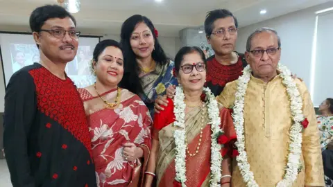 Sapna Mukherjee Sougat (second from right) at a family celebration. He is joined in the picture (from left to right) by his elder brother, Sourav Mukherjee, Sourav's wife Nupur, Sapna and his parents Soma and Syamal. They are all wearing traditional Indian dress and Sougat's parents have flower garlands around their necks.