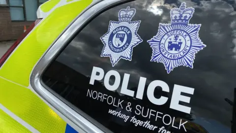 Ben Parker/BBC A close up of a police car window with the Norfolk and Suffolk police emblems on it.