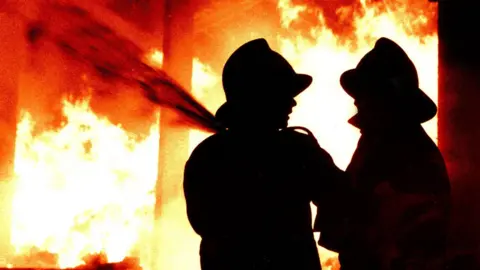 BBC Firefighters with a hose and fire in the background