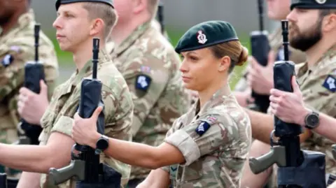 Junior officers in the Royal Army Medical Corps holding rifles and dressed in camouflage.