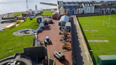 An aeriel view of the Heugh Battery Museum in Hartlepool. 
In the centre there is a selection of war tanks, in the background you can see the sea.
