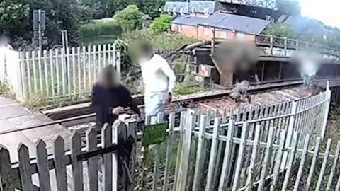 Network Rail Four people running from right to left along a railway track. There is white fencing running either side of the tracks