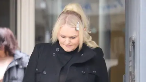 Hollie Dance leaving Southend Crown Court wearing a black coat. She has long blonde hair.